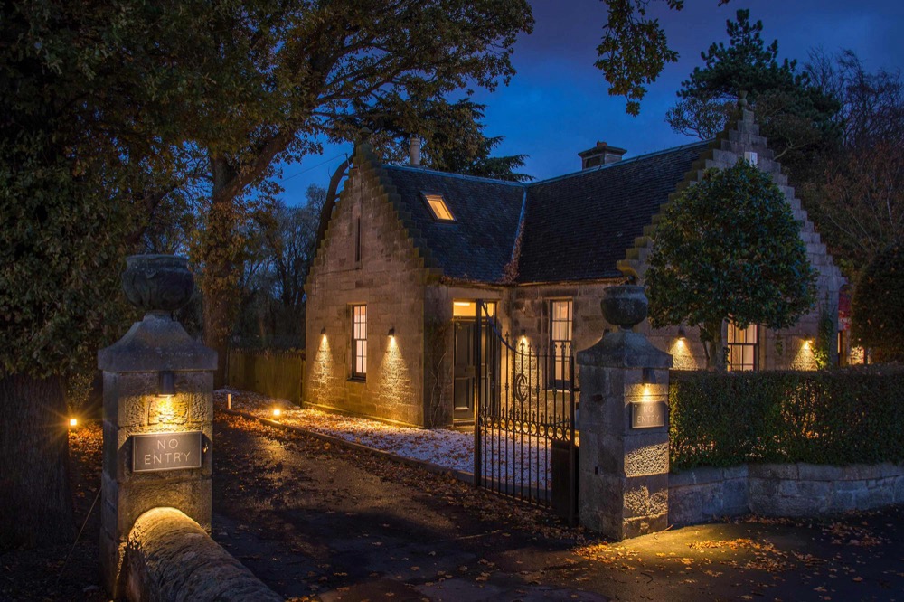 The Gate Lodge at Carlowrie at dusk, lit warmly behind its iron gates