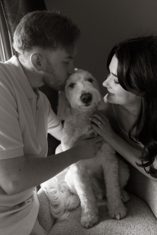 Kaylee and David kissing Monty between them, by the window